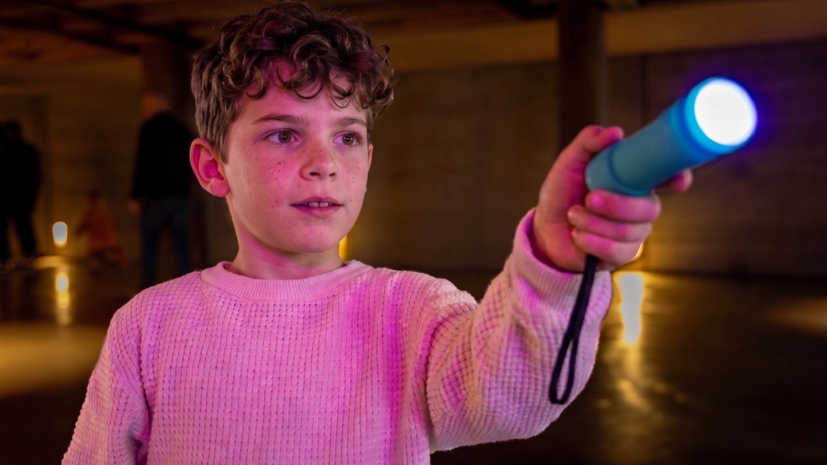 Boy holding up a torch in a darkened room.