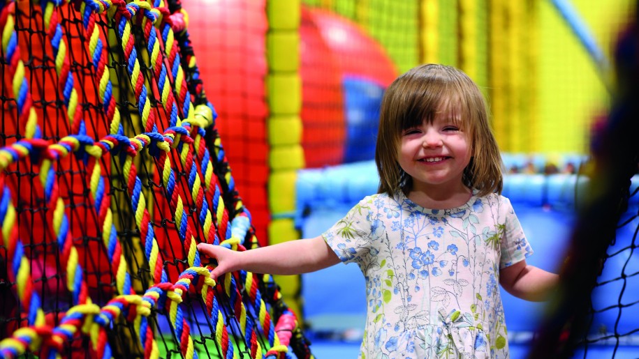 Laughing small child negotiating a rope net bridge at a soft play centre.
