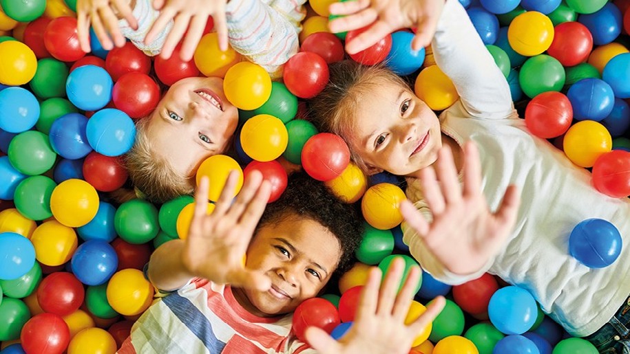 Three smiling children in a ball pool at a soft play centre.