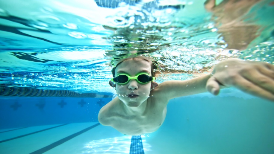 Child in green goggles swimming underwater.