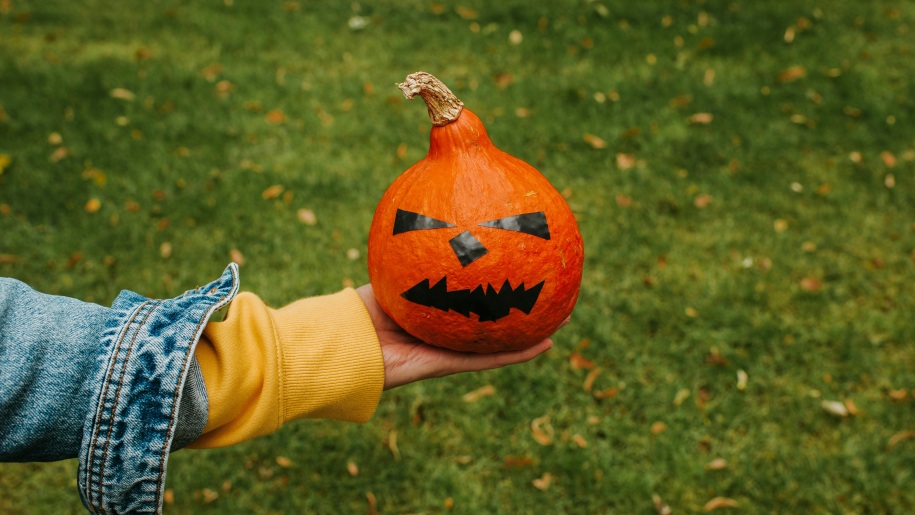 A hand holding a mini pumpkin decorated with stickers to make a spooky face.