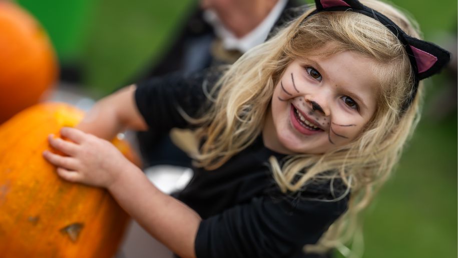 Girl dressed up as a black cat for Halloween and a pumpkin.
