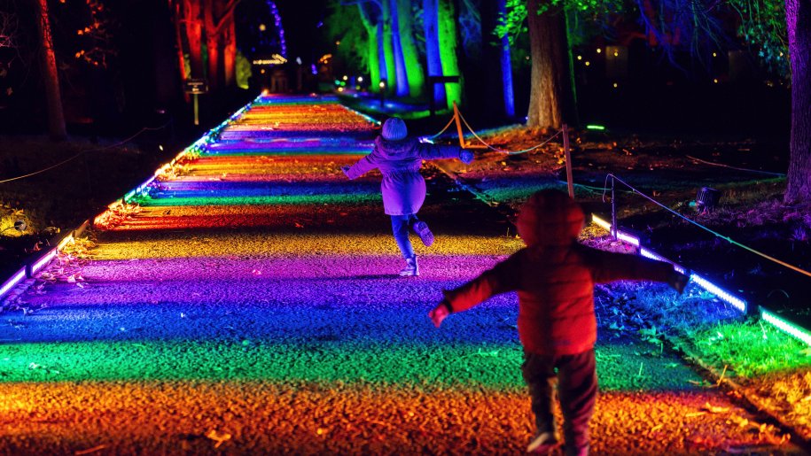 Two children skipping down a multi-coloured illuminated path.
