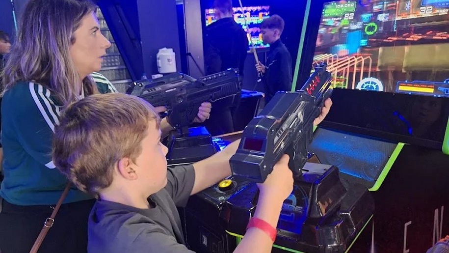 Woman and boy playing a shooting game at an indoor arcade.