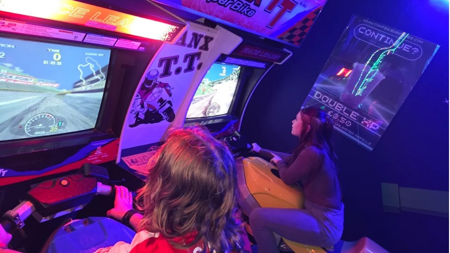 Young people playing a motorcycle racing simulator game at an indoor arcade.