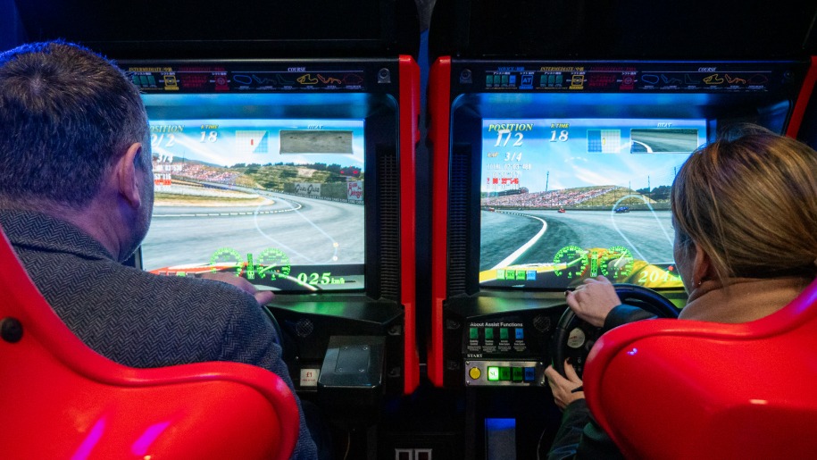 Two adults playing on a racing car simulator at an indoor arcade.