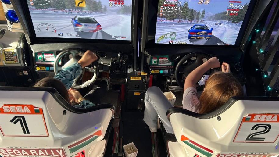 Two children playing a racing car game at an indoor arcade.