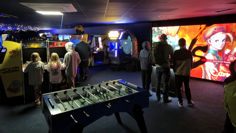 Children and adults playing on various machines at an arcade.