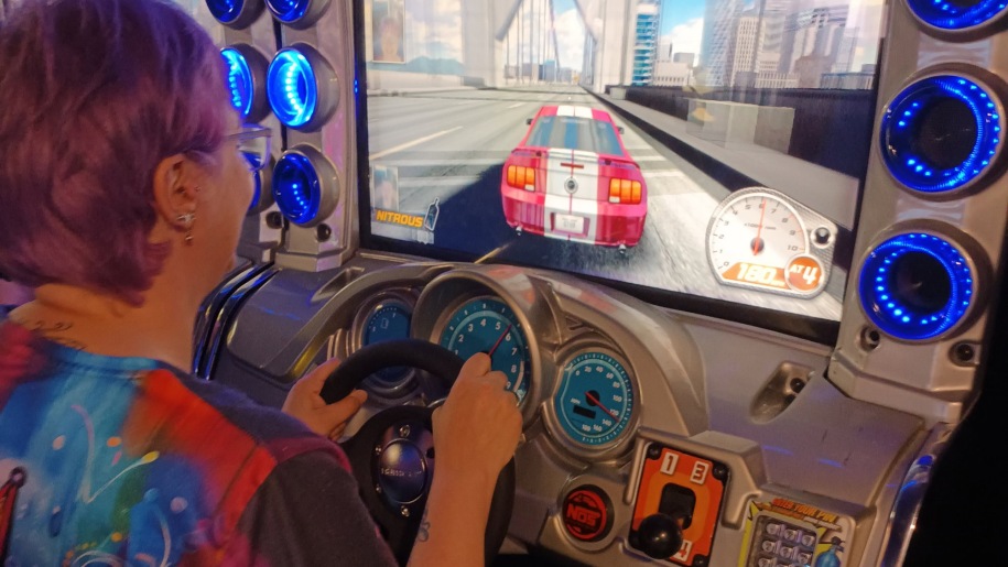 Woman playing a car racing game on a machine at an arcade.