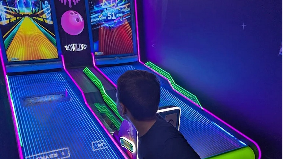 Boy playing a bowling game on an arcade machine.