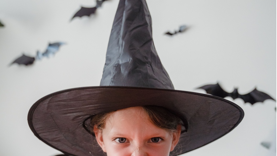 Halloween child wearing a pointed black witch's hat with bats in the background.