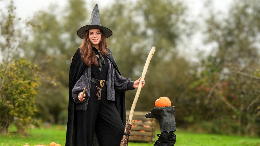 Woman dressed as a witch with broomstick and pumpkin.