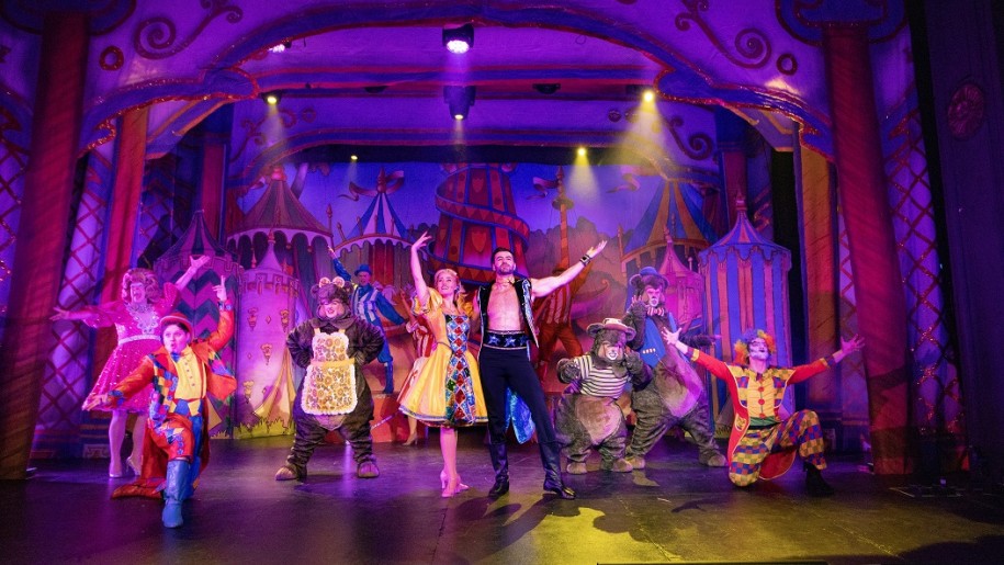 Pantomime performers on stage with circus-themed scenery.