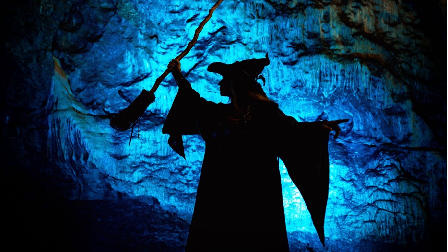 Silhouette of a witch holding a broomstick against a blue illuminated backdrop.