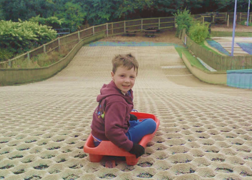 Child on a red toboggan at the top of the dry ski slope at Ackers Adventure in Birmingham.